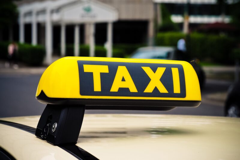 Yellow Taxi Sign, with black writing on top of car