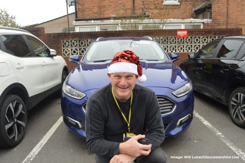Singing cabbie in front of his taxi wearing a Christmas hat to spread cheer