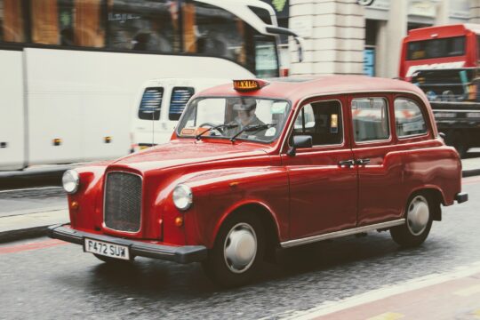 vintage style red hackney carriage on a busy road